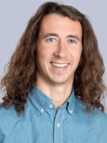 Portrettfoto, mann, smil, skulderlangt brunt hår, blå skjorte