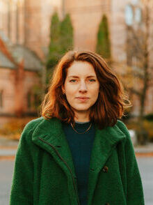 Portrettfoto, kvinne, smil, brunt skulderlangt hår, grønn jakke, utendørs
